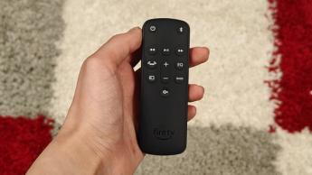 Пульт дистанционного управления для саундбара Amazon Fire TV в руке над красно-бело-серым ковром