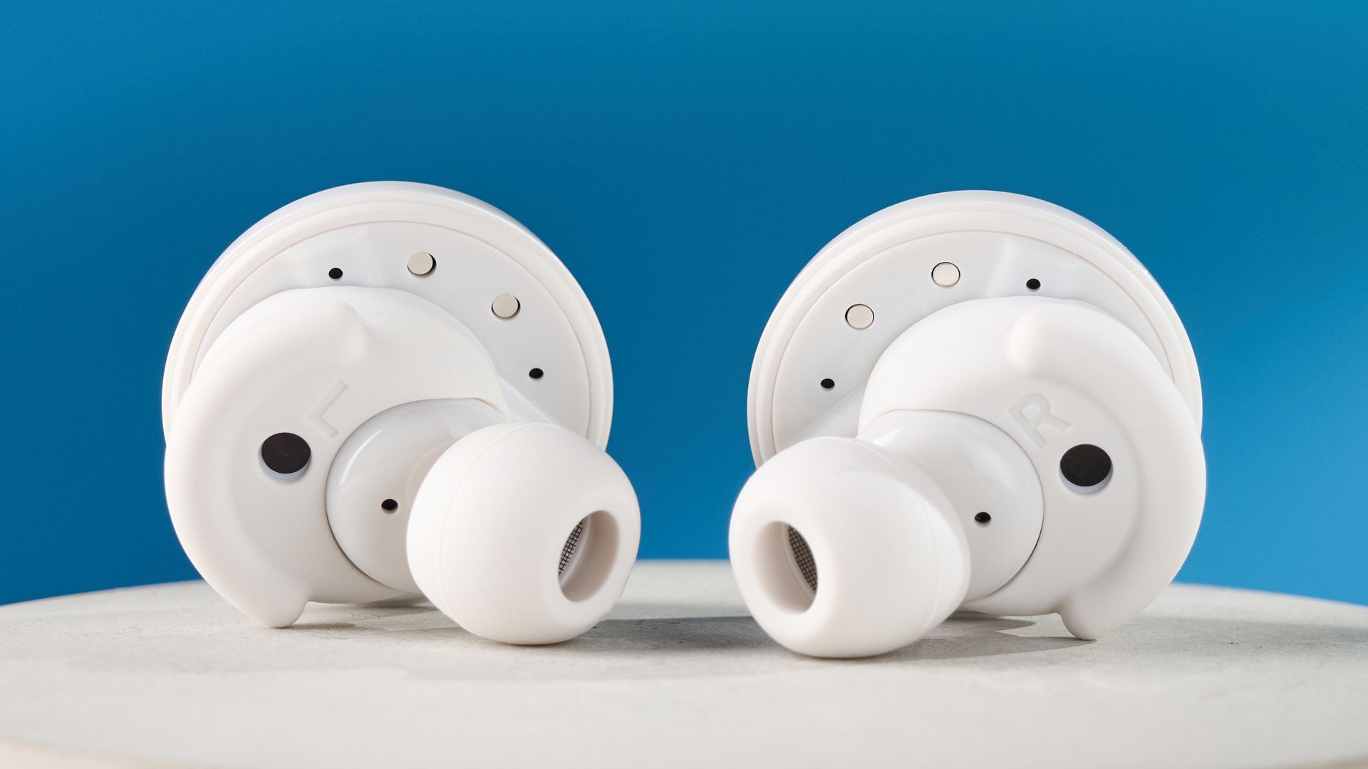 Weiße Denon perL Pro True-Wireless-Ohrhörer mit runden Ohrstöpseln und passender weißer Ladehülle vor blauem Hintergrund