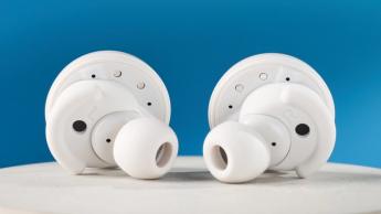 Weiße Denon perL Pro True-Wireless-Ohrhörer mit runden Ohrstöpseln und passender weißer Ladehülle vor blauem Hintergrund