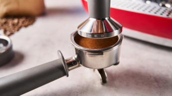 Uma máquina de espresso vermelha da Smeg com moedor de grãos, sobre um fundo azul