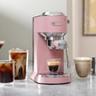 A máquina de espresso De'Longhi Dedica Duo na cor rosa sobre uma bancada de cozinha com bebidas à base de café