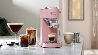 A máquina de espresso De'Longhi Dedica Duo na cor rosa sobre uma bancada de cozinha com bebidas à base de café