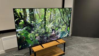 Телевизор Sony Bravia 9 mini LED на деревянной тумбе, отображающий яркий лесной пейзаж