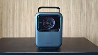 Домашний кинотеатр-проектор Nebula X1 на чёрном деревянном столе, на фоне деревянные стены