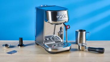 La macchina per espresso Breville Bambino Plus in acciaio inox argento con accessori, tra cui bricco per il latte, pressino e portafiltro, mostrata durante l’estrazione dell’espresso su sfondo blu