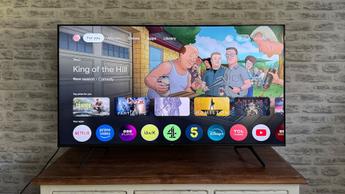 Умный телевизор TCL C6KS с диагональю 50 дюймов на фоне кирпичной стены, на экране домашняя страница Google TV с сериалом «Царь горы»