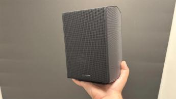 Тыловая колонка Samsung HW-Q990F в руке на фоне серой стены