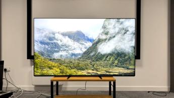 Телевизор Sony Bravia 9 Mini LED на деревянной тумбе, на экране — горный пейзаж с облаками