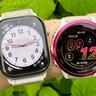 Foto close-up Apple Watch 10 dan Garmin Forerunner 570 yang diletakkan berdampingan