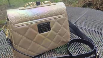 Bolsa crossbody dorada Loungefly Sanrio 50 aniversario exhibida sobre una mesa