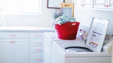Lave-linge à chargement par le dessus blanc avec un panier rouge dans une buanderie