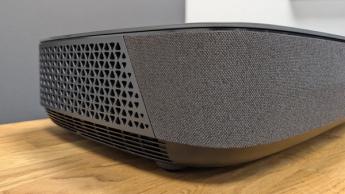 Крупный план ультракороткофокусного проектора Hisense PL2: боковая решётка и тканевая текстура на деревянном столе