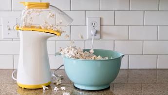 Máquina de palomitas desbordando palomitas en un tazón color aqua sobre una encimera de cocina