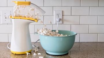 Máquina de palomitas desbordando palomitas en un tazón color aqua sobre una encimera de cocina