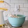 Mesin popcorn meluap, mengeluarkan popcorn ke dalam mangkuk berwarna aqua di atas meja dapur