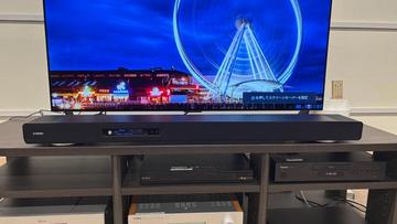 Саундбар Yamaha True X Surround 90A с тыловыми колонками и сабвуфером, установленный в простой комнате с телевизором