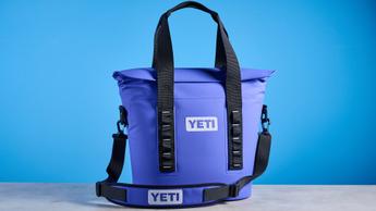 Bolsa isotérmica Yeti Hopper M15 con asa acolchada, asas y una capacidad de 15 cuartos, presentada con latas de Coca-Cola Zero sobre un fondo azul