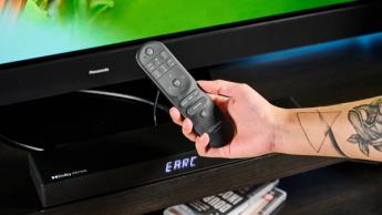 the ultimea nova s50 a black compact soundbar with LED on the front and a wired subwoofer is photographed on a black TV mount connected to a panasonic TV