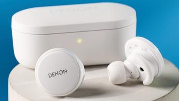 Weiße Denon perL Pro kabellose Ohrhörer mit runden Earbuds und passender weißer Ladebox auf blauem Hintergrund