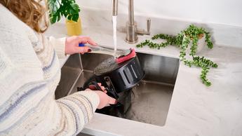 Pessoa limpando uma air fryer em uma cozinha moderna branca