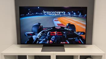 OLED-телевизор Samsung S90F с диагональю 48 дюймов, показывающий вид из кокпита болида Формулы-1, установлен на белой деревянной мебели