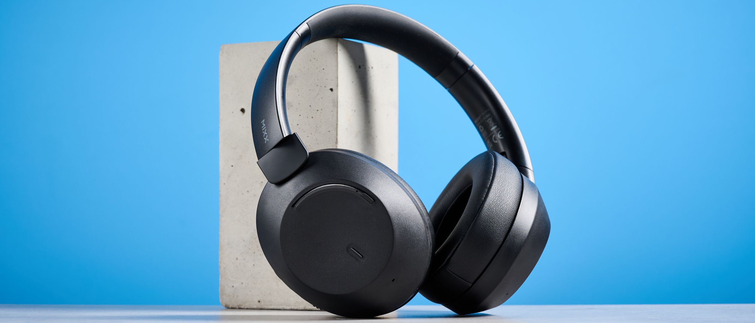 Mixx StreamQ C4 kabellose Kopfhörer in Schwarz mit weichen Ohrpolstern und Bedientasten vor blauem Hintergrund