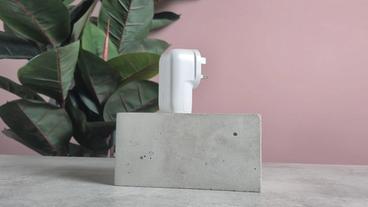 Cargador de pared Belkin BoostCharge USB-C de 3 puertos con PPS 67W mostrado sobre un bloque con fondo rosa y una planta