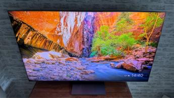 ЖК-телевизор TCL 65C8K, снятый под небольшим углом сверху, отображает природный пейзаж с ручьём и деревьями