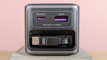 Primer plano del power bank Ugreen Nexode de 20.000 mAh y 165 W mostrando los puertos y el cable USB-C retraído sobre un escritorio con fondo rosa