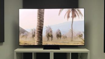 OLED-телевизор Samsung S95F на белой деревянной тумбе показывает ярких динозавров и пальмы