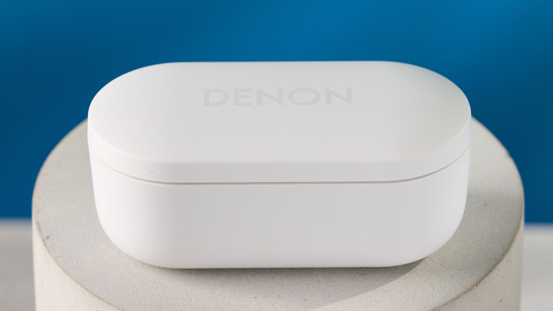 Denon perL Pro True-Wireless-Kopfhörer in Weiß mit rundem Design und passender weißer Ladehülle auf blauem Hintergrund