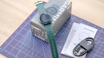 Close-up of the Garmin Vivoactive 6 smartwatch in green sitting on top of its box next to a charging cable and paperwork on the device