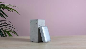 Aukey Spark Mini 20000 bærbar oplader på et skrivebord med en lyserød væg og en grøn plante i baggrunden