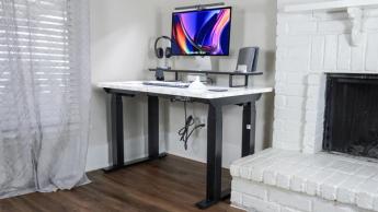 Escritorio elevable FlexiSpot E7 Plus colocado en una esquina junto a una chimenea