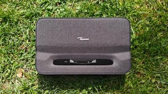 Вид сверху на портативный ультракороткофокусный проектор Optoma Photon Go на зеленой траве, выделены объектив и логотип Optoma