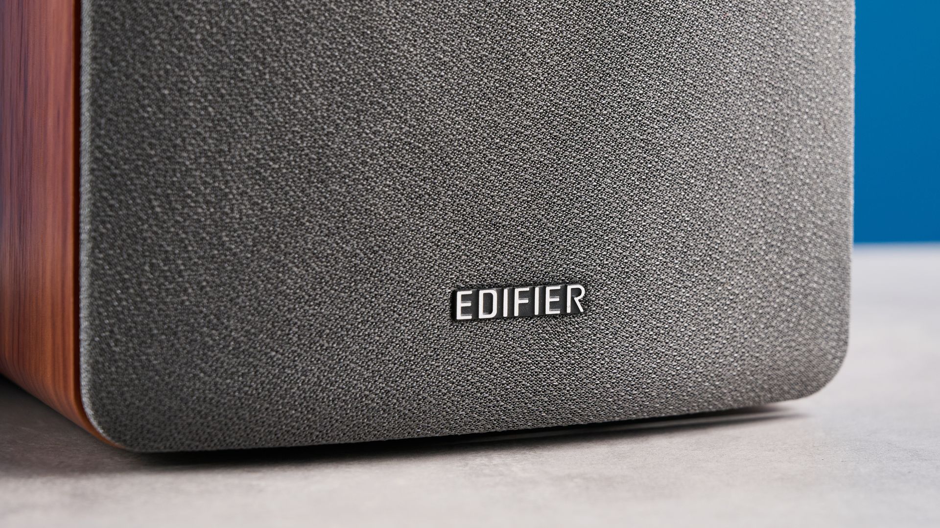 Die Edifier R1280T Regallautsprecher in Holzoptik vor blauem Hintergrund, mit Fokus auf Lautstärkeregler, Lautsprechertreiber, Hochtöner, RCA- und AUX-Eingänge sowie Fernbedienung