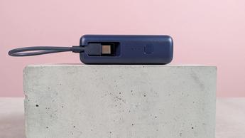 Vista en primer plano del cable de carga integrado en la batería externa Xiaomi de 33 W y 10.000 mAh, colocada sobre un escritorio con fondo rosa.