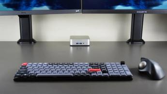 Geekom A6 mini-PC placerad bakom ett skrivbord med dubbla skärmar, mekaniskt tangentbord och styrkulemus