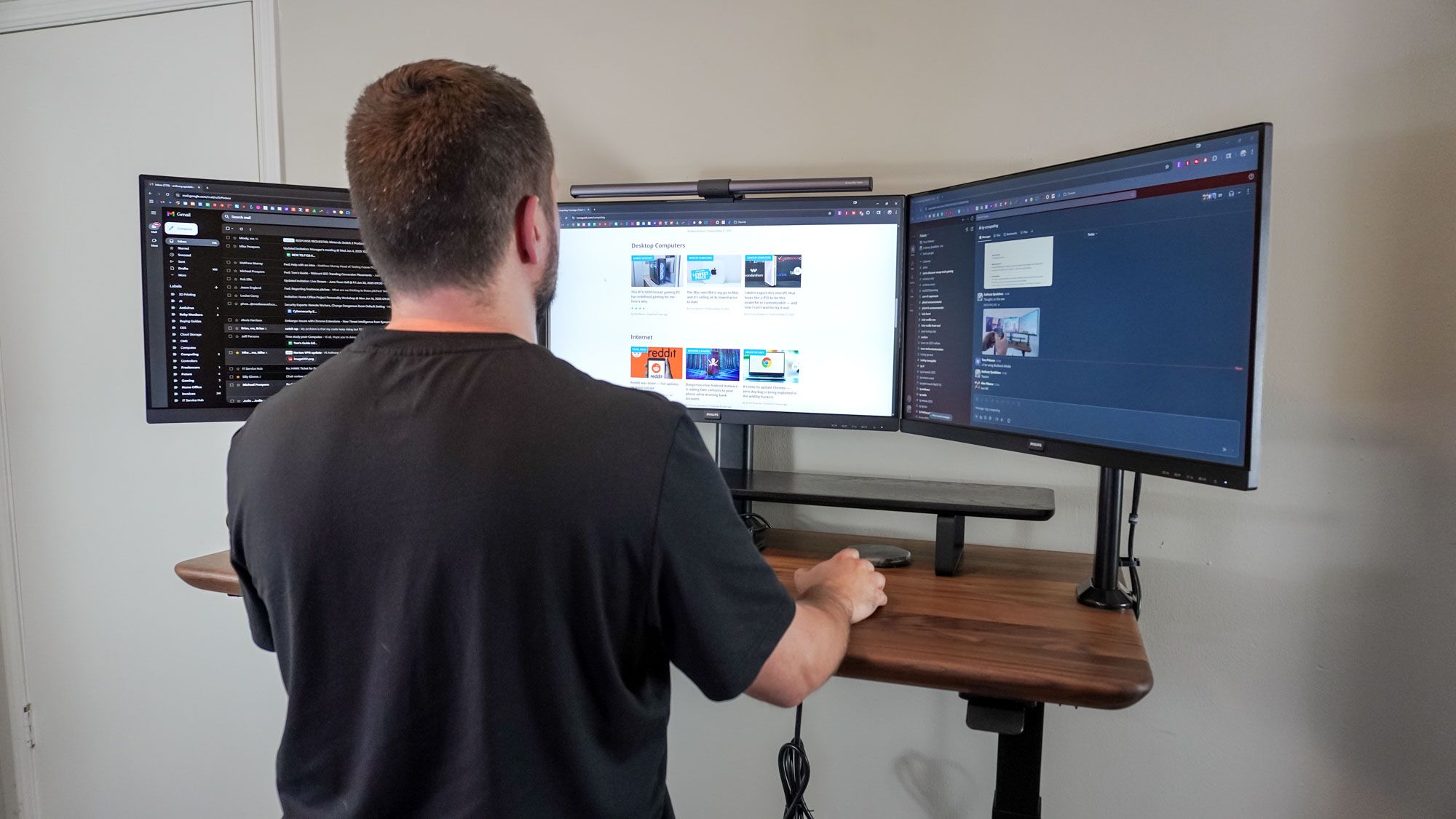 オフィスのワークスペースで、スタンディングデスクと3台のモニターを使っている人