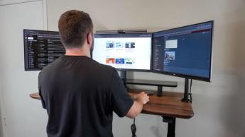 현대식 사무실에서 스탠딩 데스크와 세 대의 모니터를 사용하는 사람