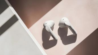 Hvide Denon AH-C500W open-ear høretelefoner hviler på en lyserød og grå overflade