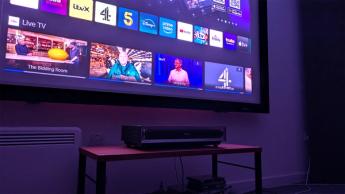 Короткофокусный проектор Hisense PX3 на деревянной стойке с отображением домашней страницы смарт-ТВ Vidaa на экране