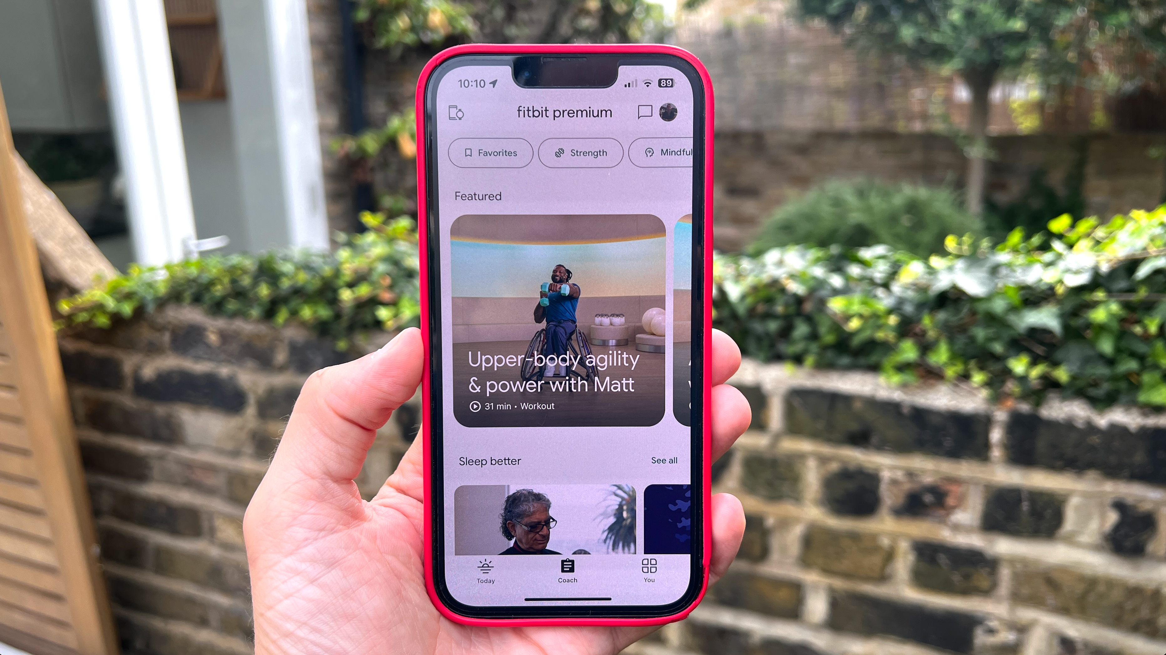 En person som håller en iPhone med Fitbit Premium-panelen visad i Fitbit-appen