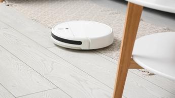Robot aspirador blanco moviéndose por un suelo de madera blanca