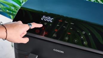 Uma fritadeira elétrica Cosori preta com dois cestos transparentes, luzes internas, grelhas para cozimento e espetos para churrasco incluídos