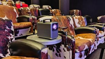 Проектор Nebula X1 стоит на металлическом столе в кинозале с креслами в анималистичном стиле