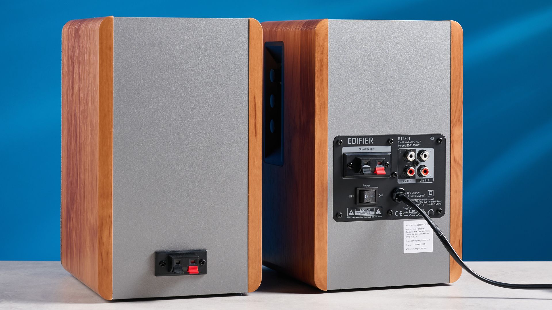 Die Edifier R1280T Regallautsprecher in Holzoptik vor blauem Hintergrund, mit Fokus auf Lautstärkeregler, Lautsprechertreiber, Hochtöner, RCA- und AUX-Audioeingänge sowie Fernbedienung