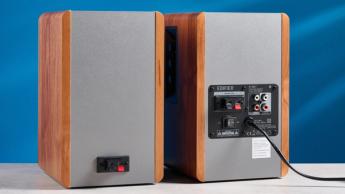 Die Edifier R1280T Regallautsprecher in Holzoptik vor blauem Hintergrund, mit Fokus auf Lautstärkeregler, Lautsprechertreiber, Hochtöner, RCA- und AUX-Audioeingänge sowie Fernbedienung