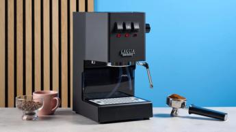 A máquina de espresso Gaggia Classic E24 Evo Pro com acessórios incluídos exibidos sobre uma superfície de pedra com fundo azul