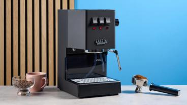 La macchina per espresso Gaggia Classic E24 Evo Pro con accessori inclusi esposta su un piano in pietra e sfondo blu